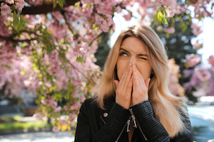Kvinna som lider av säsångsbetonad pollenallergi nära ett blommande träd utomhus